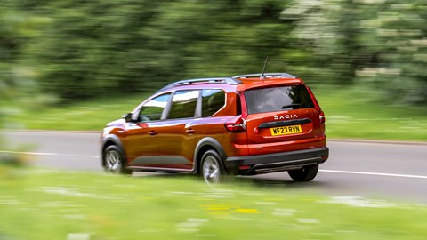 Dacia Jogger Hybrid (2023): rear three quarter driving, motion blur, country lane, orange car