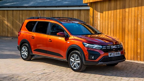 Dacia Jogger Hybrid (2023): front three quarter static, sheds in background, orange car