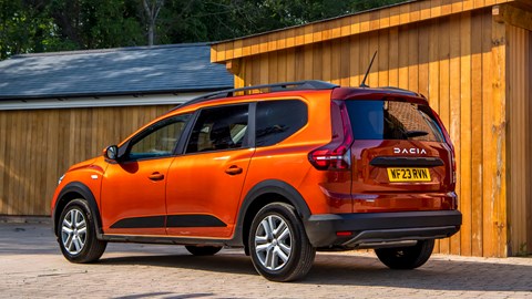 Dacia Jogger Hybrid (2023): rear three quarter static, sheds in background, orange car