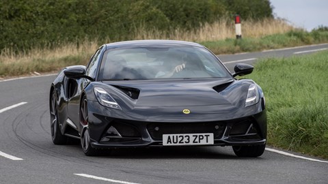 Lotus Emira (2023): front three quarter cornering, black paint, country lane