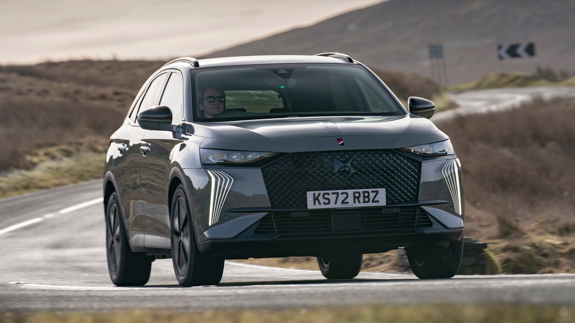 DS 7 (2023) review: front cornering shot, grey car, arid background, showing body roll