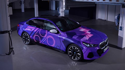 BMW i5: frente de três quartos, ângulo alto, envoltório inspirado em videogame