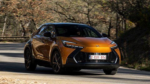 Toyota C-HR PHEV (2024) review: front three quarter cornering, shadowed by trees, orange and black paint, French roads