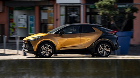 Toyota C-HR PHEV (2024) review: side view driving, orange and black paint, French roads, next to Marina