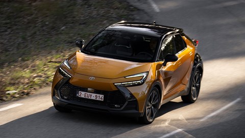 Toyota C-HR PHEV (2024) review: front three quarter cornering, high angle, shadowed by trees, orange and black paint, French roads