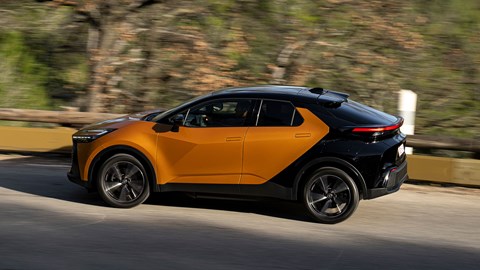 Toyota C-HR PHEV (2024) review: rear side view cornering, shadowed by trees, orange and black paint, French roads