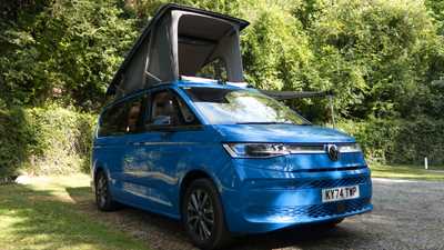 Image of a blue Volkswagen California with roof raised in a wooded campsite