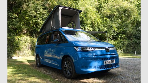 Image of a blue Volkswagen California with roof raised in a wooded campsite