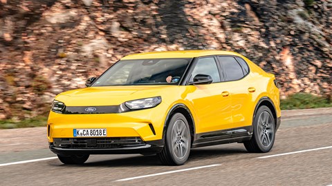 Ford Capri (2024) review: rear three quarter driving, yellow paint, hill in background