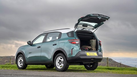 Rear three-quarter view of a teal Vauxhall Frontera SUV with its boot open, showing outdoor gear inside, parked in the countryside.