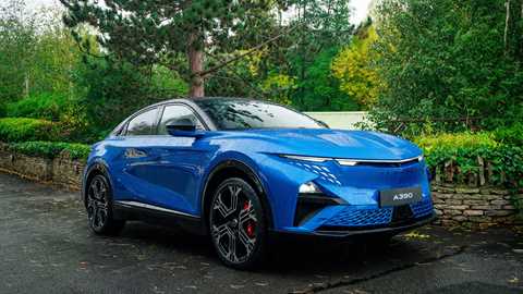 A blue Alpine A390 2025 on a rainy day in front of a leafy green backdrop