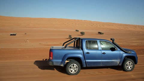 VW Amarok driving in the desert, passing a camel